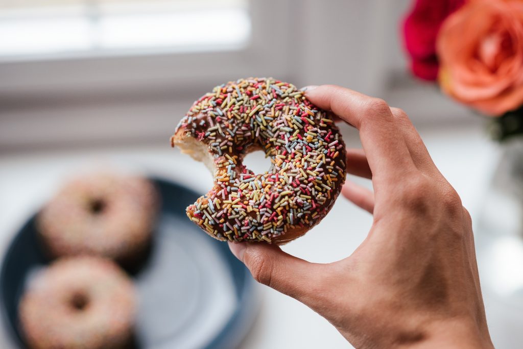 A hand holding a donut covered in chocolate and sprinklesthat has been bitten out of.