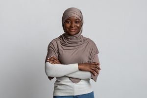 Confident black muslim woman posing with folded arms over light background