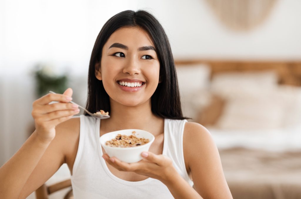 Happy asian woman holding bowl with oatmeal