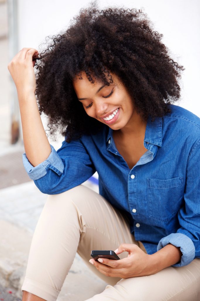 Portrait of happy black woman sitting with mobile phone